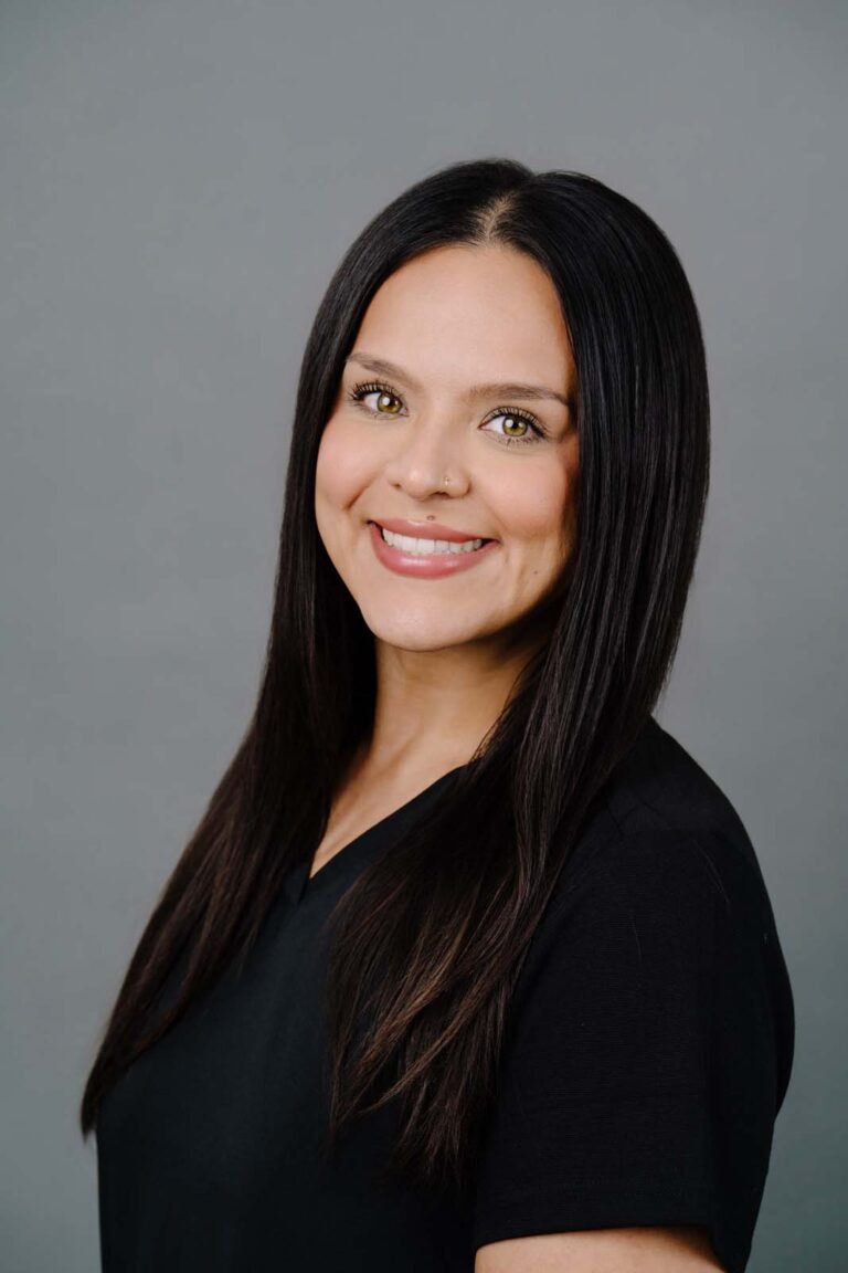 Head shot of a dentist from Missouri City Dentistry wearing a black scrubs and smiling. The background is a plain gray color.