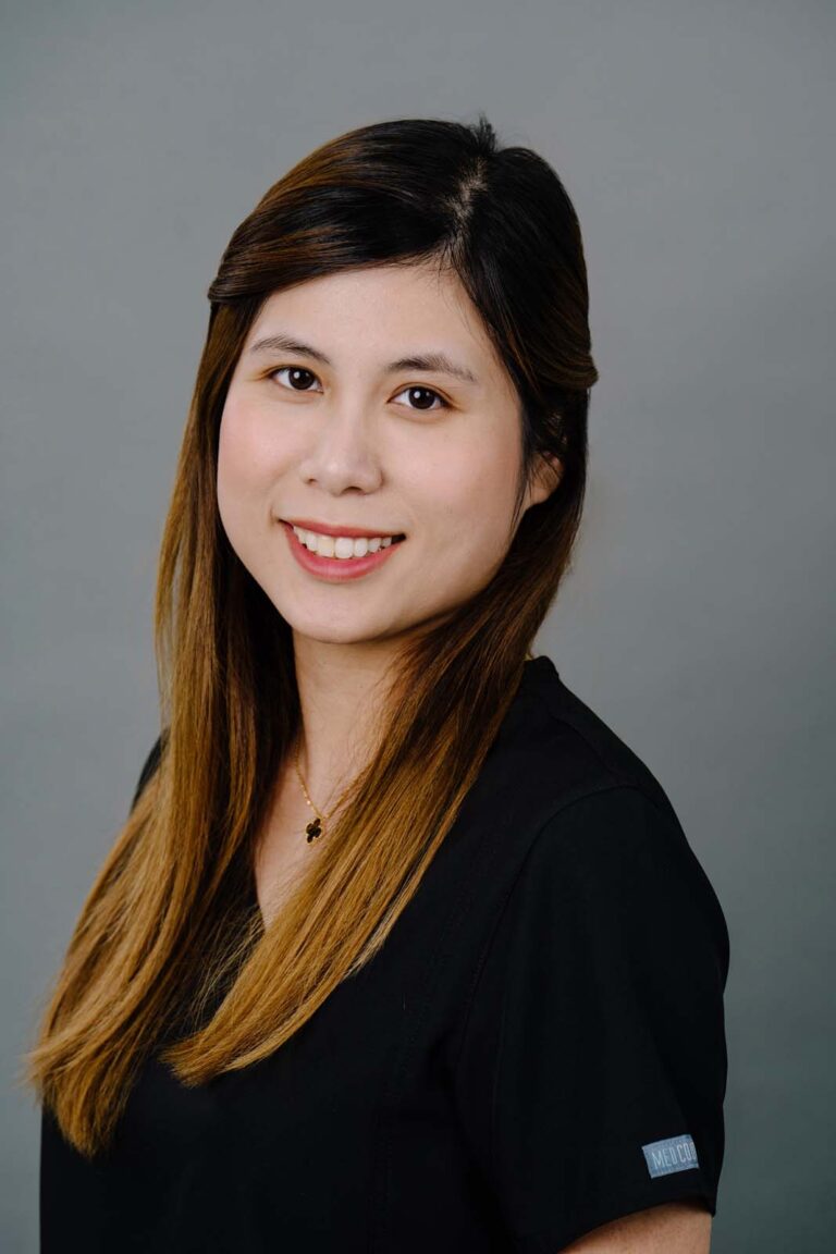 Head shot of a dentist from Missouri City Dentistry wearing a black scrubs. The background is a plain gray color.