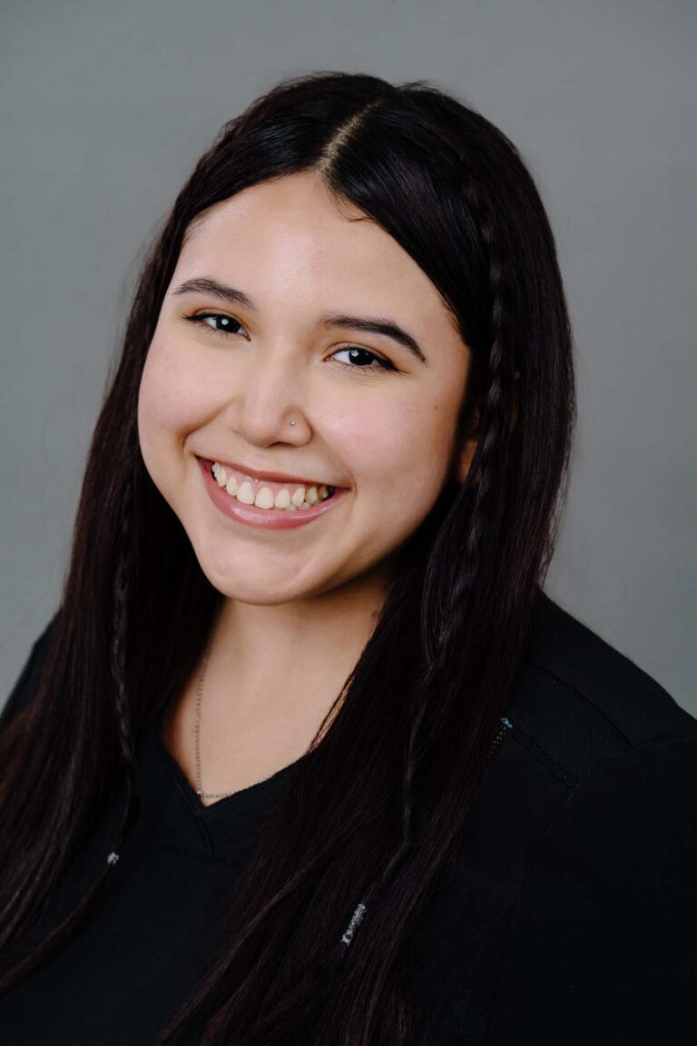 Head shot of a dentist from Missouri City Dentistry wearing a black scrubs and smiling. The background is a plain gray color.