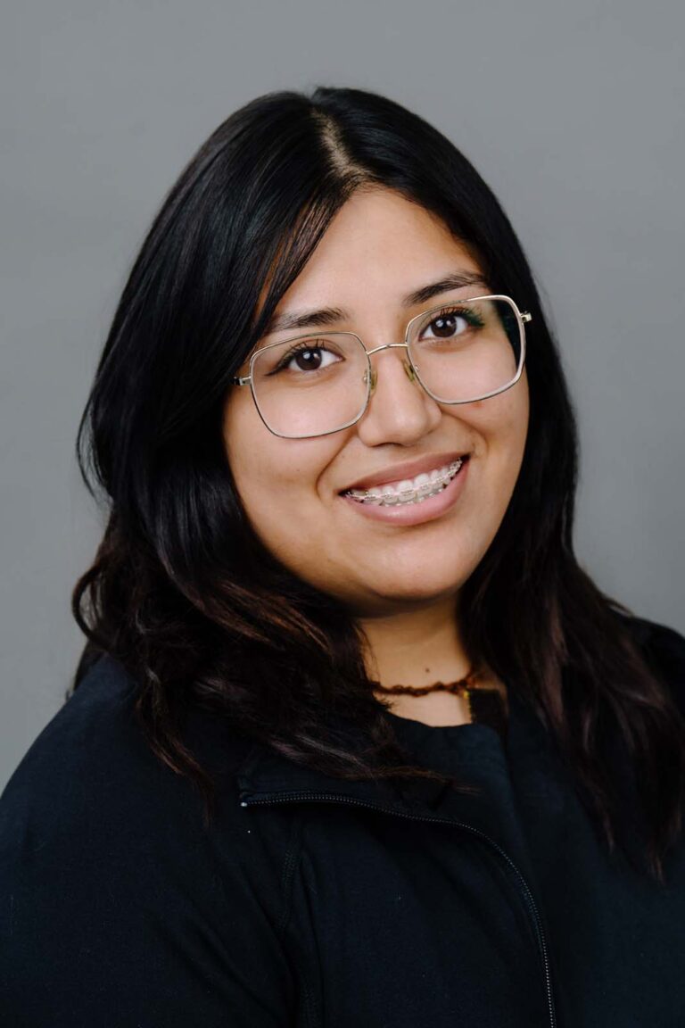 Head shot of a dentist from Missouri City Dentistry wearing a black scrubs and eye glasses. The background is a plain gray color.